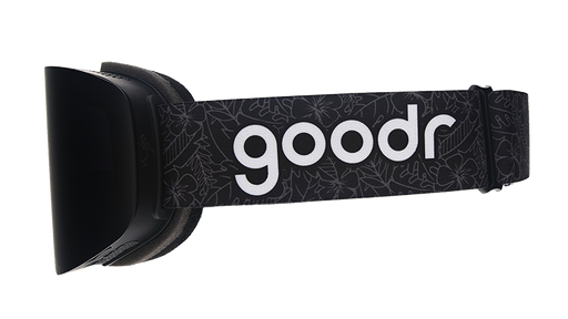 Side view of black snow goggles with an adjustable black strap with the goodr logo over a faintly outlined tropical pattern.