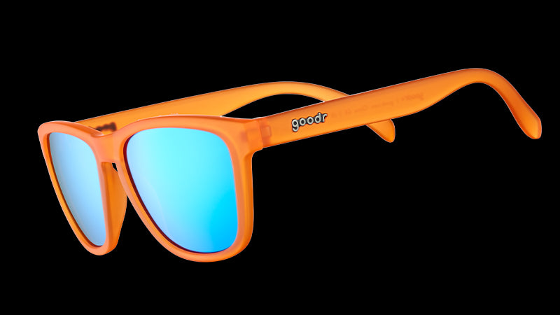 Three-quarter angle view of translucent bright orange sunglasses with blue reflective lenses on a white background.