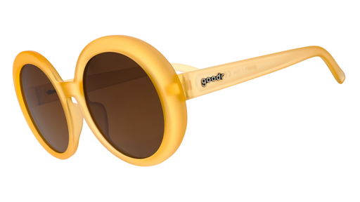 Three-quarter view of a pair of oversized, round, pale orange sunglasses with brown, non-reflective lenses.