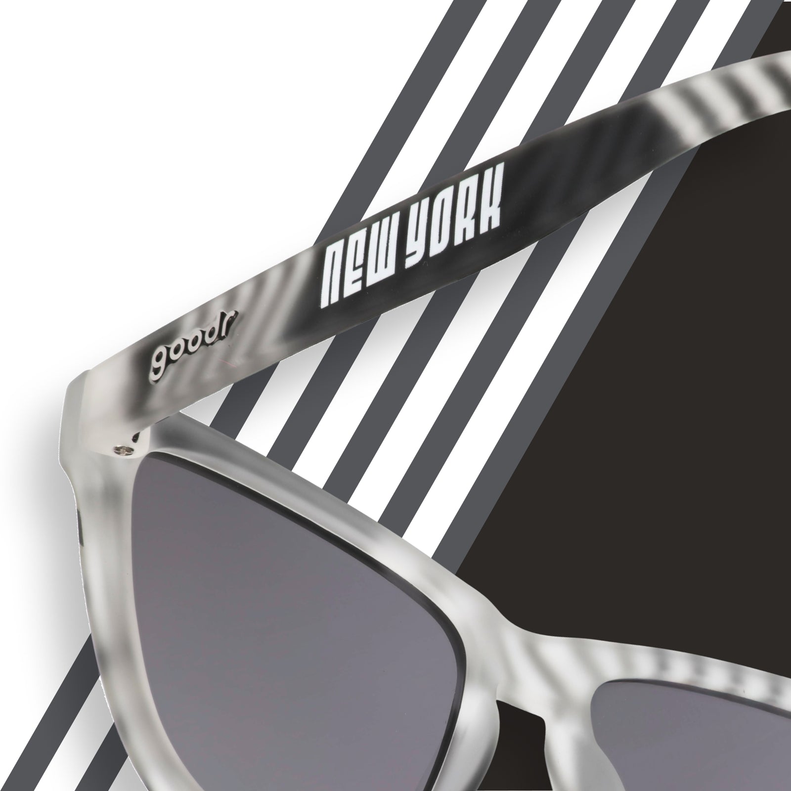 Back view of gray and black sunglasses featuring a geometric print, and a New York and goodr logo on a striped background.