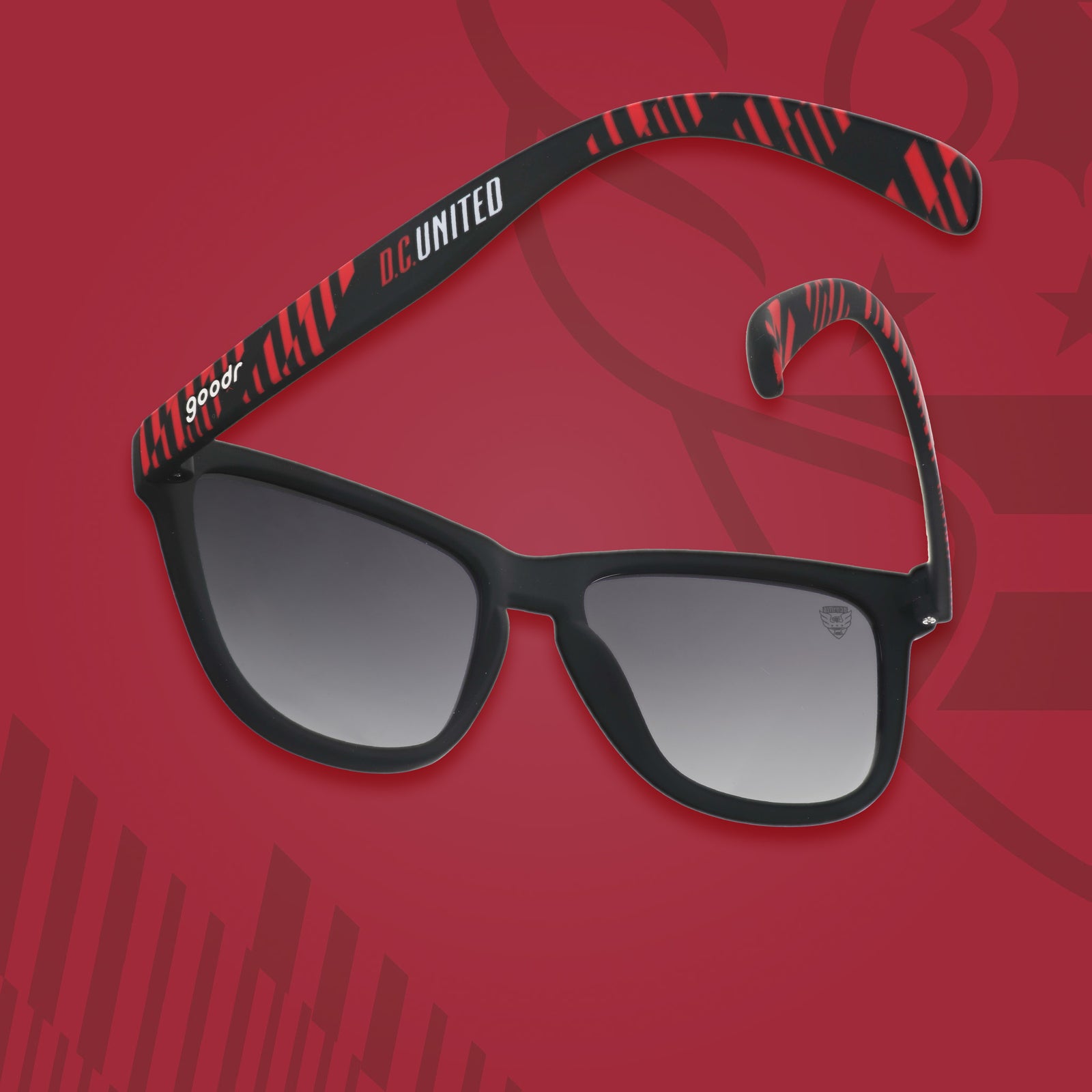 Three-quarter angle view of DC United shades tilted down. Black and red frames. Black lenses. Red background.