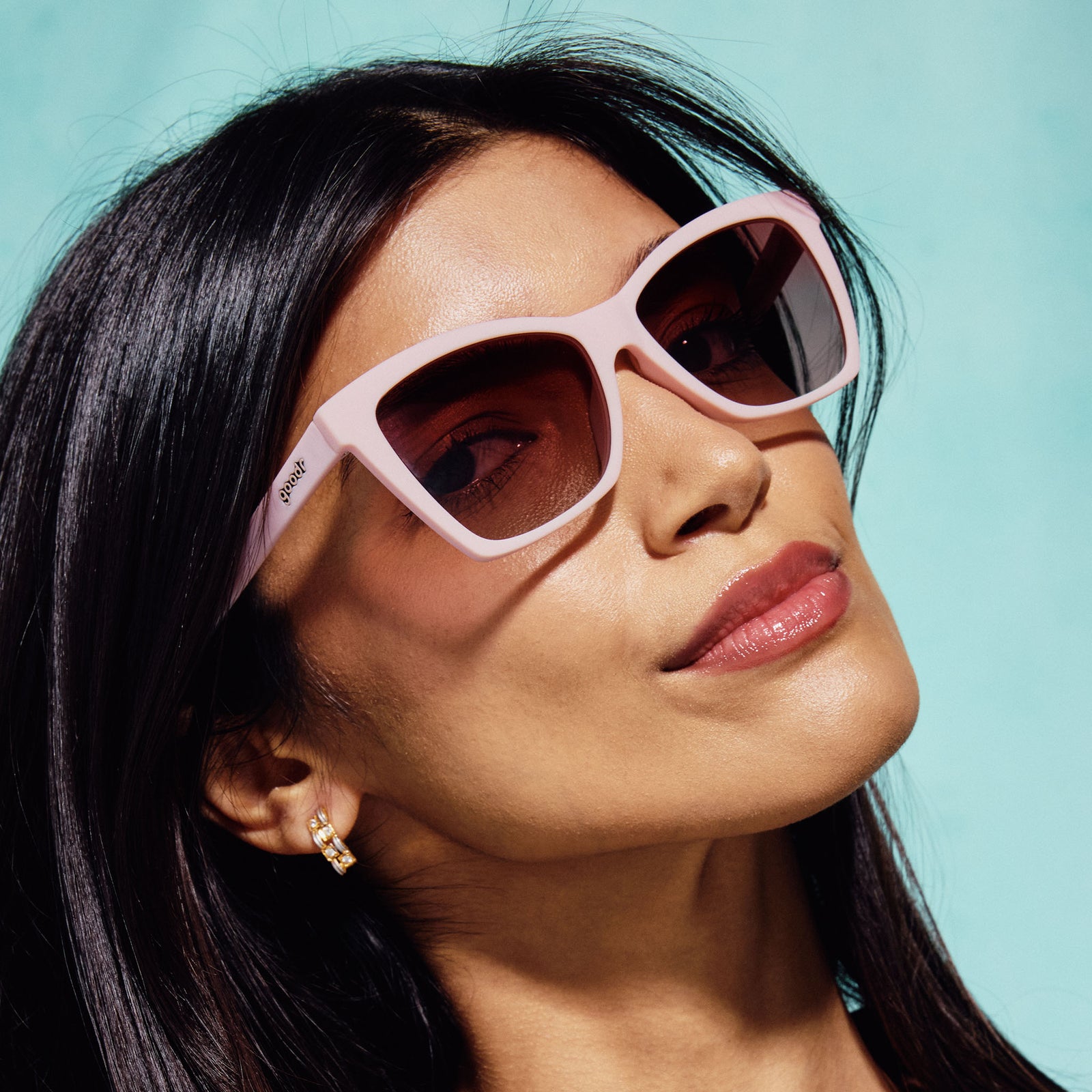 A woman wearing a pair of cat-eye sunglasses with light pink frames and rosy lenses.