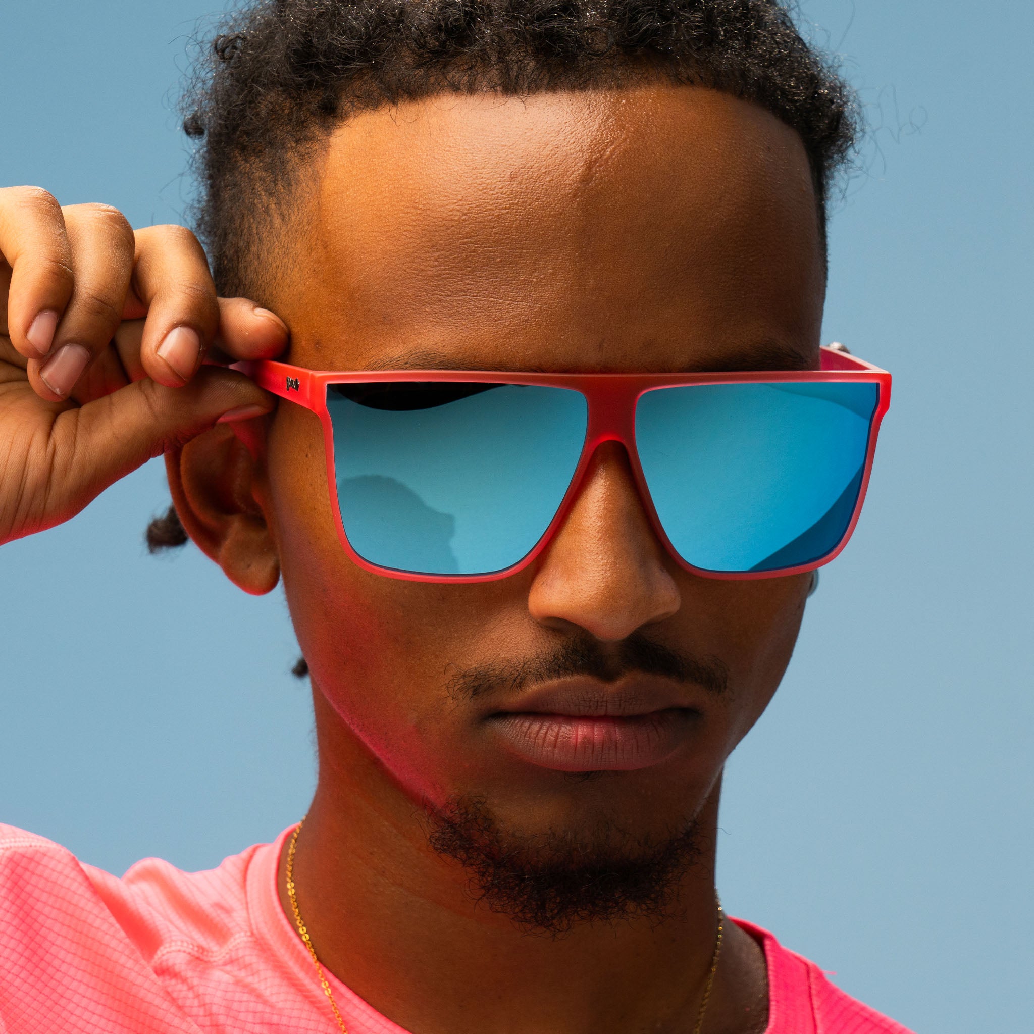 Close-up of a man with a no-nonsense expression wearing oversized pink flat-top glasses with blue reflective lenses.