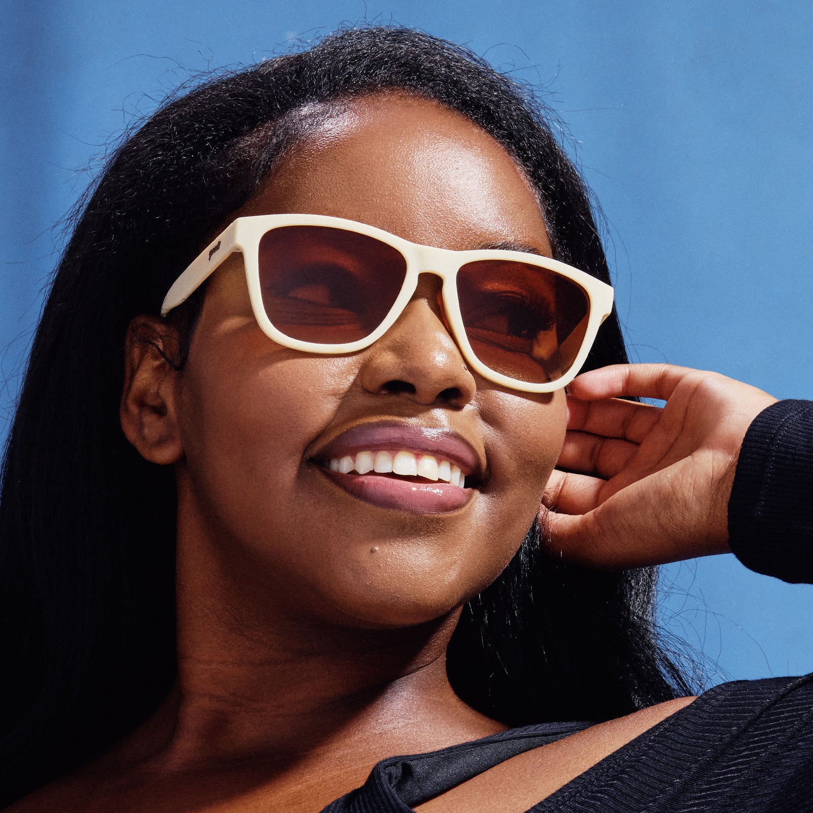 A woman wearing pair of square sunglasses with light beige frames and orange lenses.
