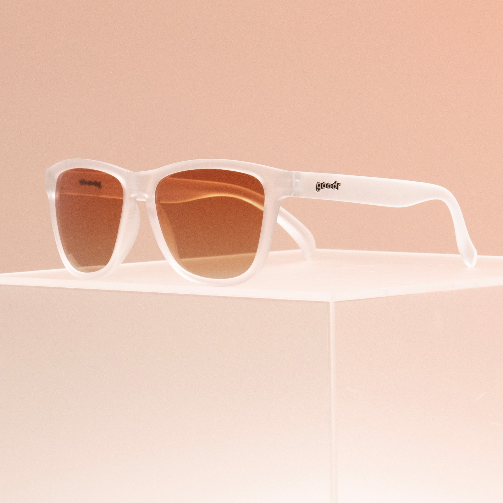 Three-quarter view of clear sunglasses with brown gradient lenses in a classic frame shape perched atop a clear box.