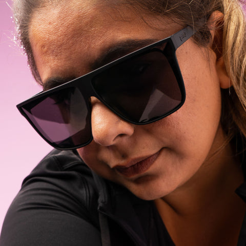 Close-up of a woman with a no-nonsense expression wearing oversized black flat-top glasses with black non-reflective lenses.