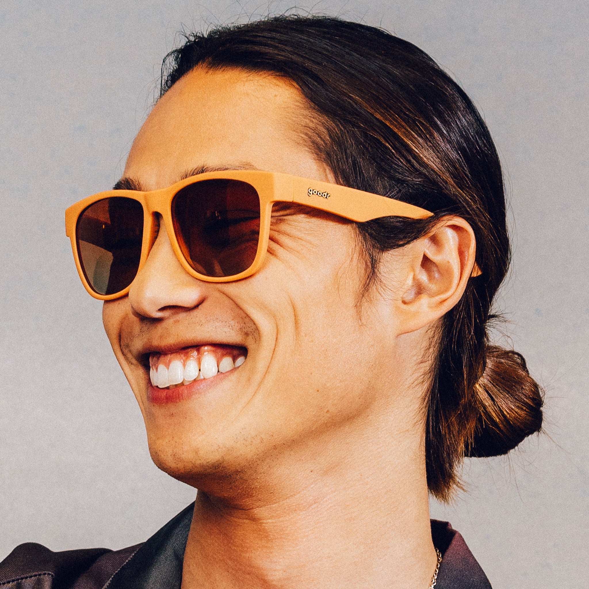 Side profile of a smiling man wearing large brown sunglasses with orange-gold gradient lenses.
