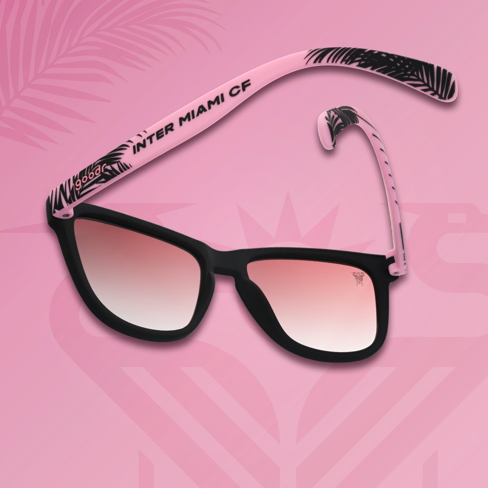 Three-quarter angle view of Inter Miami CF shades tilted down. Black and pink frames. Rose lenses. Pink background.