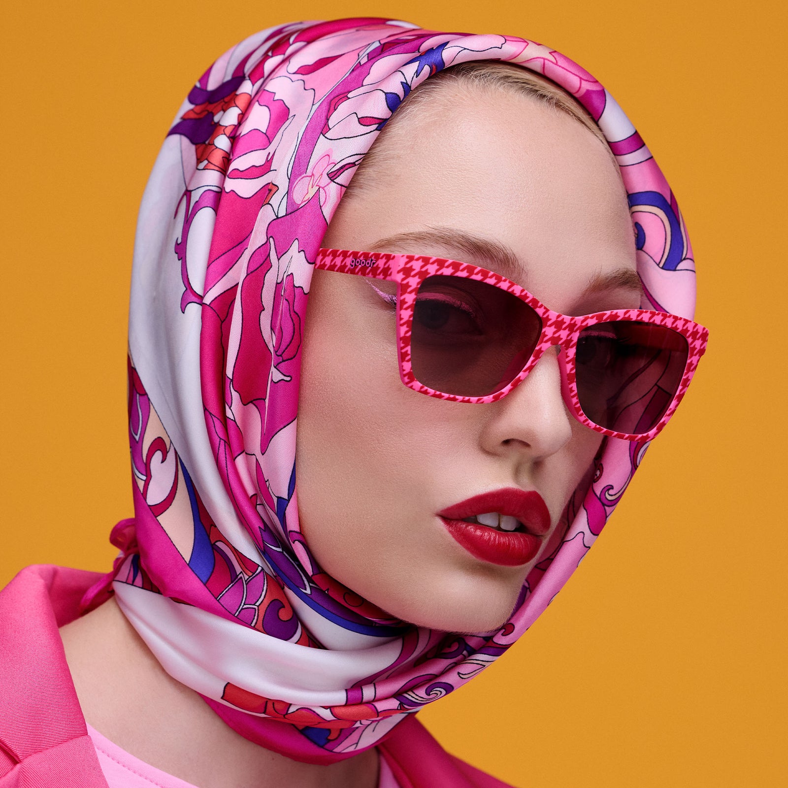 A glamorous woman in a Pucci-style silk scarf and matte red lips wears a pair of mod red and pink houndstooth print Pop Gs.