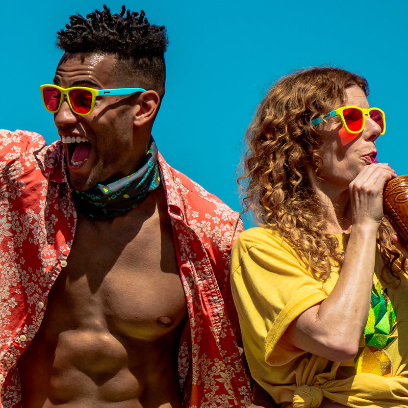 A man and woman wear light blue and yellow sunglasses with rose lenses and sip tropical drinks on a sunny day.