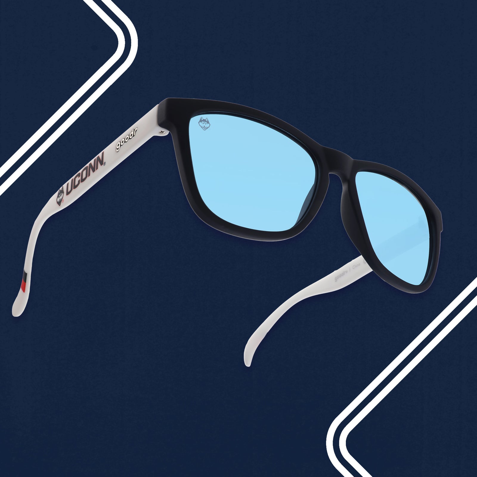 Three-quarter high-angle view of navy blue and white sunglasses with the Huskies logo and blue lenses.