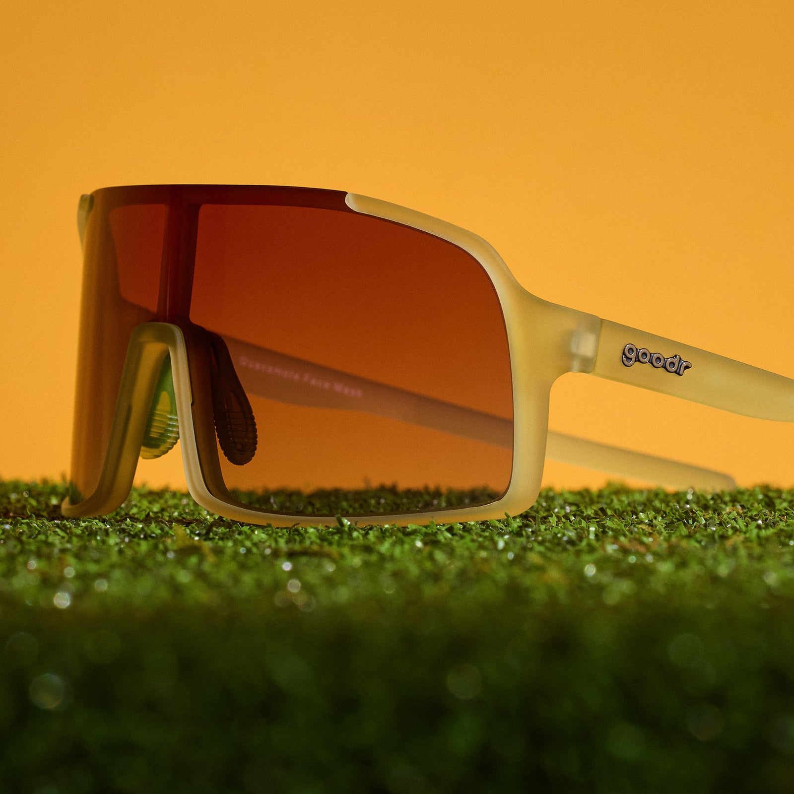 Side view of translucent chartreuse wrap sunglasses with a rose shield lens sitting atop turf.