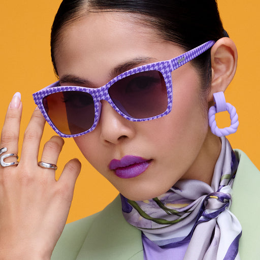 A fashionable woman in lavender and mint wears fuchsia lipstick and purple houndstooth-print Pop Gs with purple lenses.