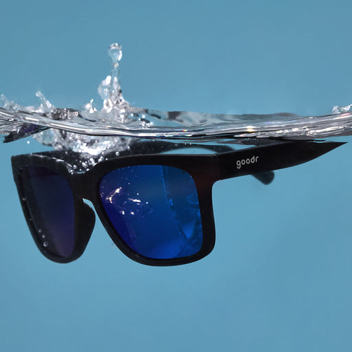 Three-quarter angle view of black sunglasses with blue lenses floating in the water after being dropped.