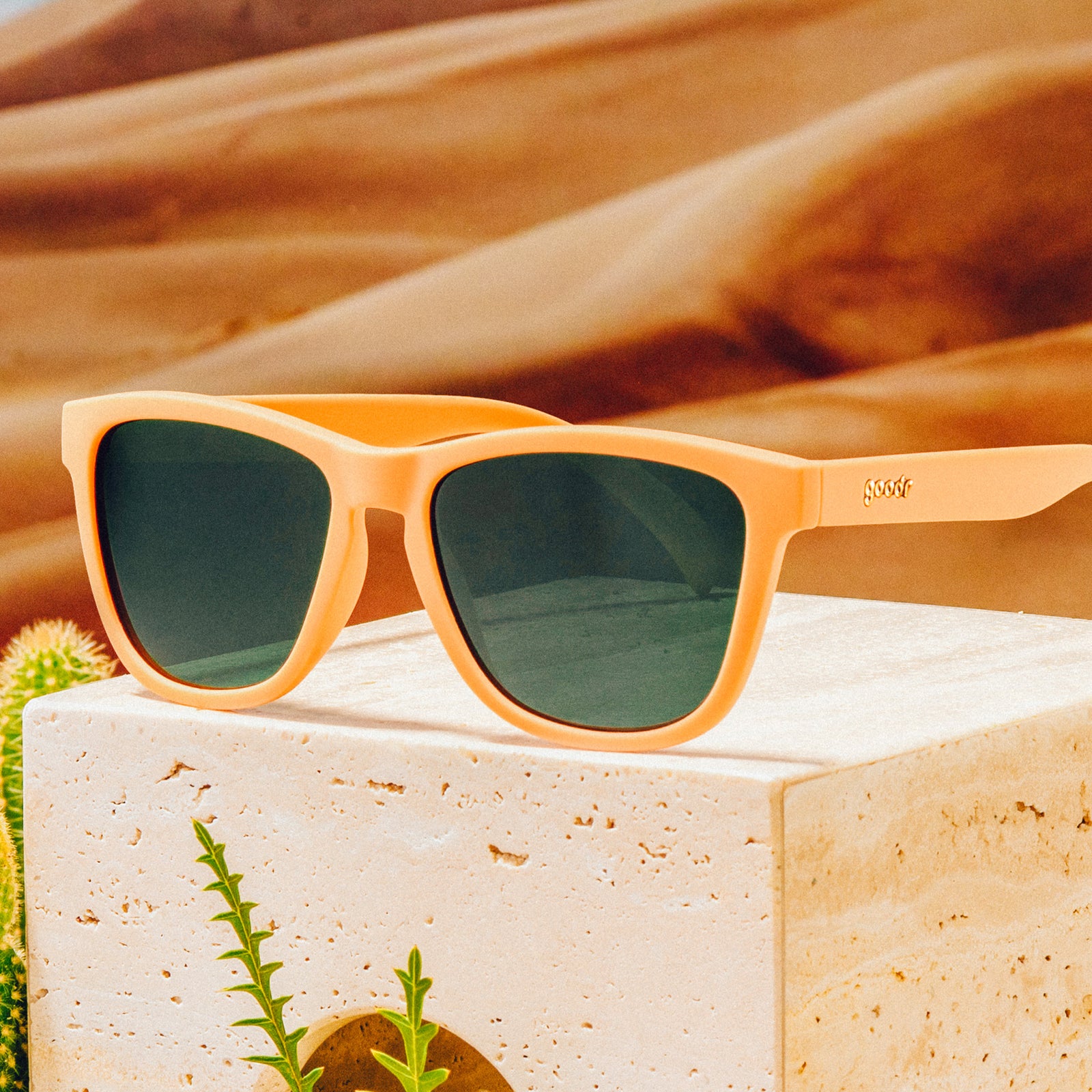 Three-quarter angle view of classic brown sunglasses with green non-reflective lenses on top of a clay block in front of a desert backdrop.