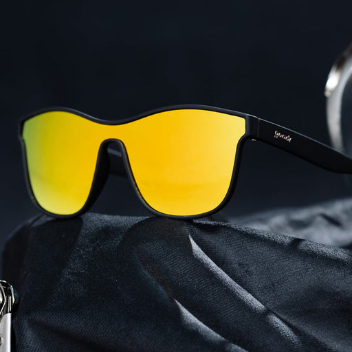 A pair of sleek black sunglasses with large, mirrored yellow lenses rests on a dark, textured fabric. The minimalist design of the frame and the bold, reflective lenses give the sunglasses a modern and stylish look.