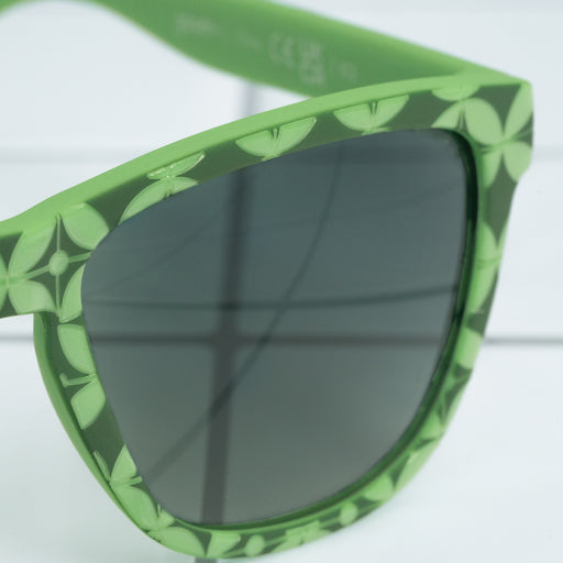 Close-up shot of the right temple of textured green-tile print sunglasses with green gradient lenses on a white tiled surface.
