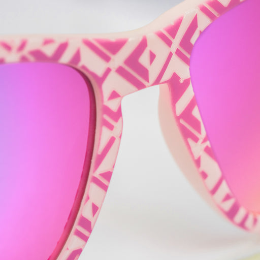 Close-up view of the center of the faceplate of a pair of textured pink tile sunglasses with purple-pink reflective lenses.