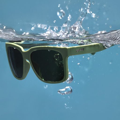 Three-quarter angle view of dark green sunglasses with green lenses floating in the water after being dropped.