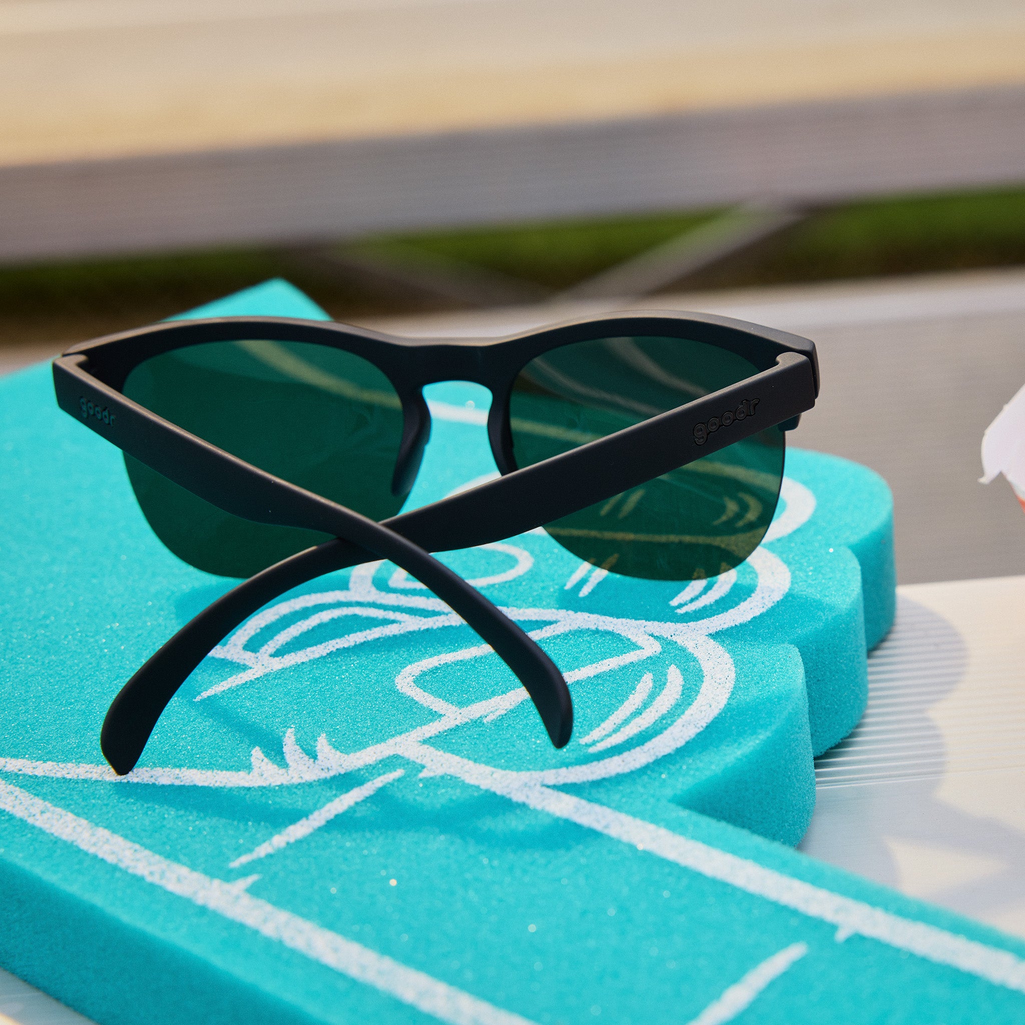 Back angle view of fashionable matte black half-rim sunglasses with non-reflective dark green lenses on bleachers.