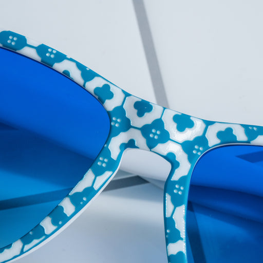 Close-up of the faceplate of blue-and-white tile-print shades with blue gradient lenses sitting on a white tiled surface.