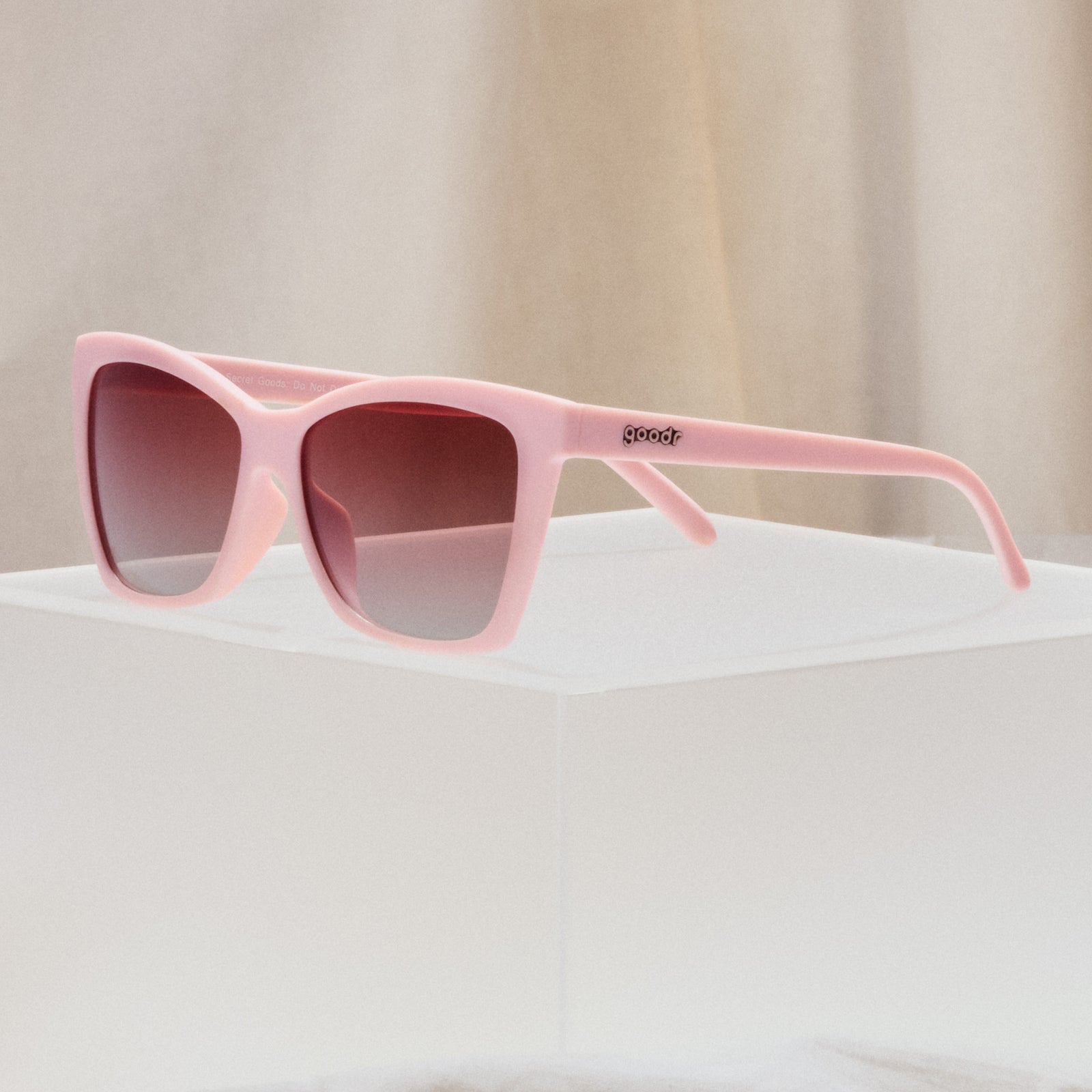 A pair of cat-eye sunglasses with light pink frames and rosy lenses.