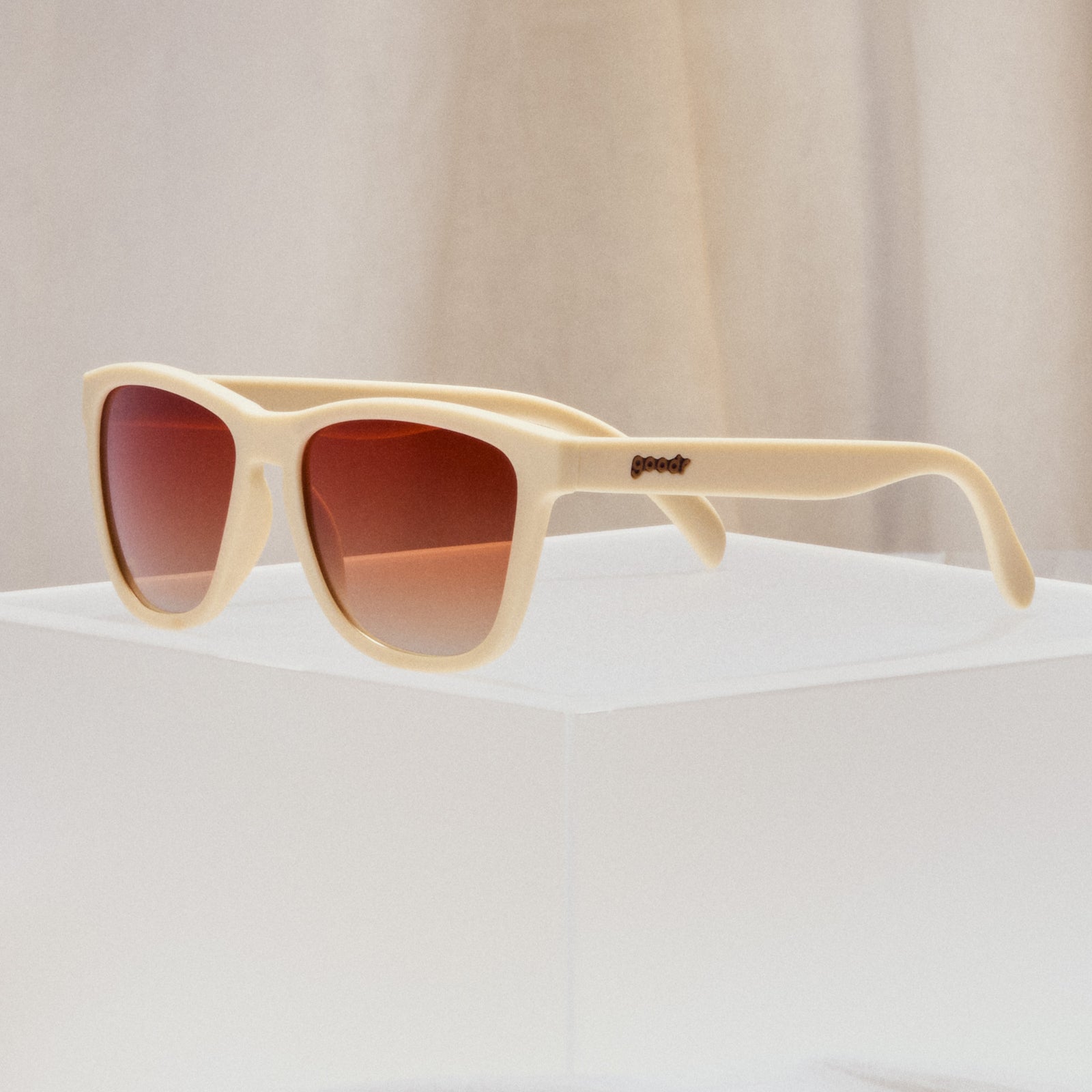 A pair of square sunglasses with light beige frames and orange lenses.