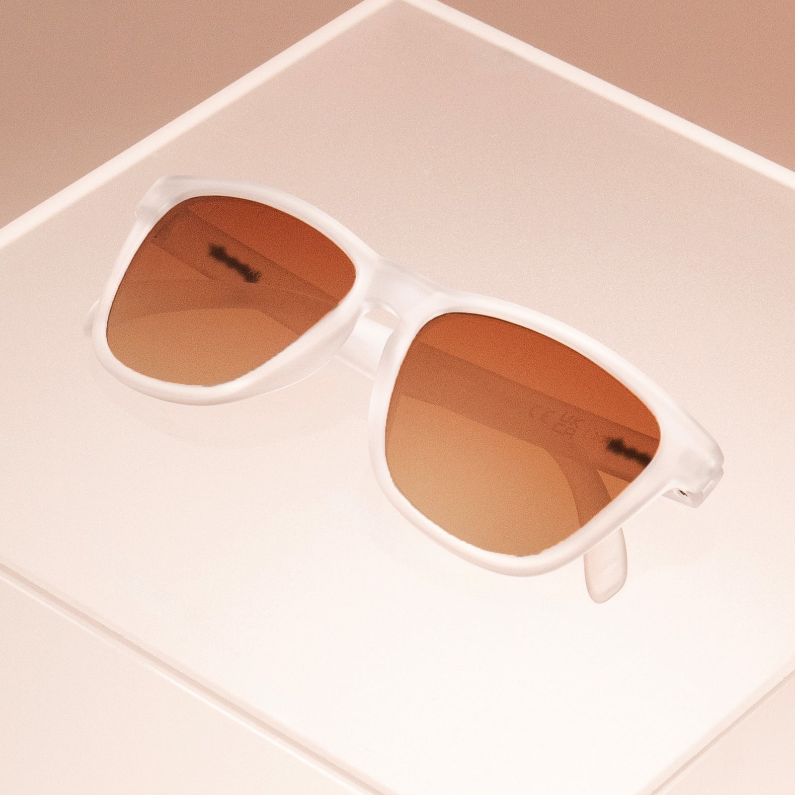Clear sunglasses in a classic frame shape with brown gradient lenses folded, sitting atop a clear plastic box.