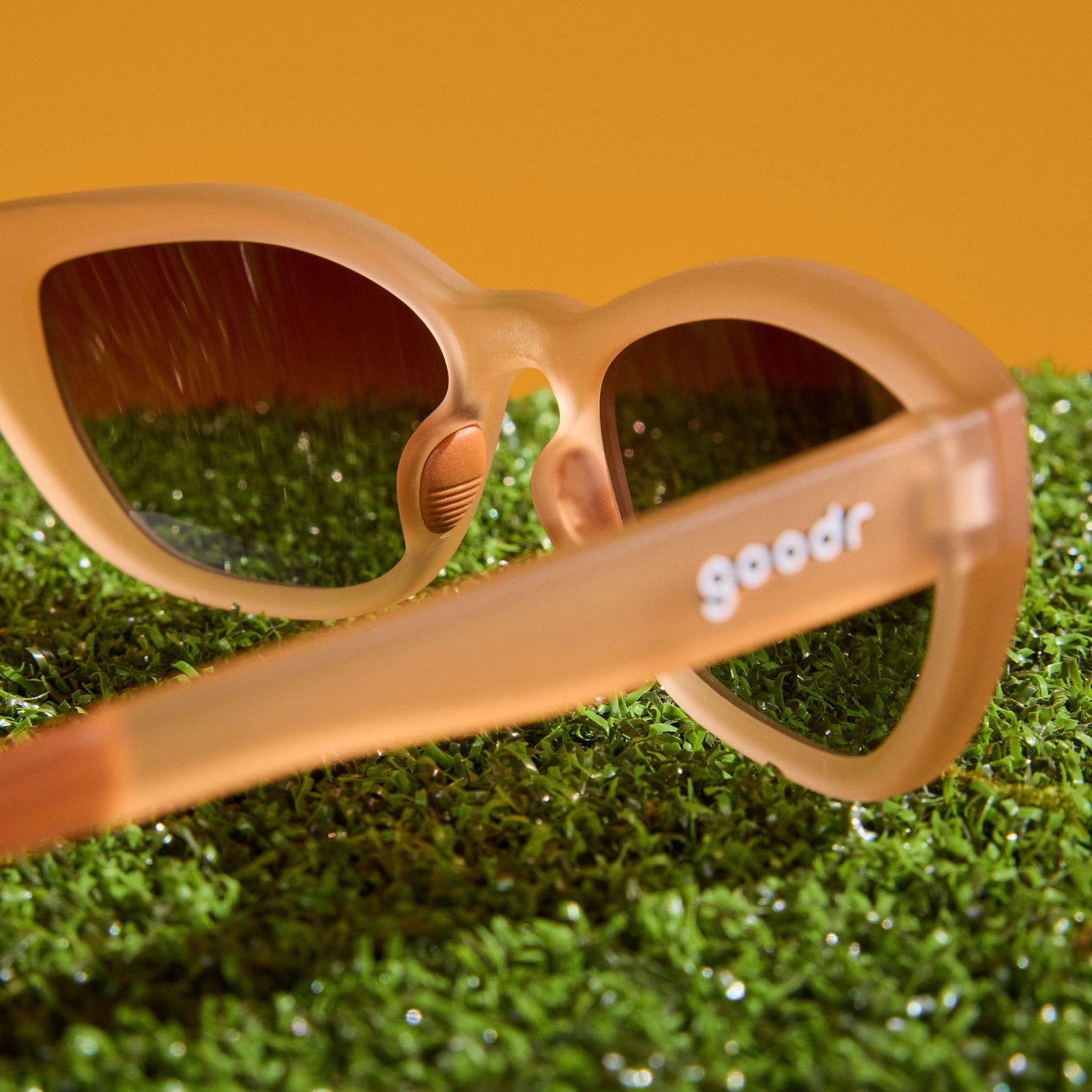 Translucent brown cat-eye Cheetah Gs photographed from behind, displayed on astroturf with a light orange background.