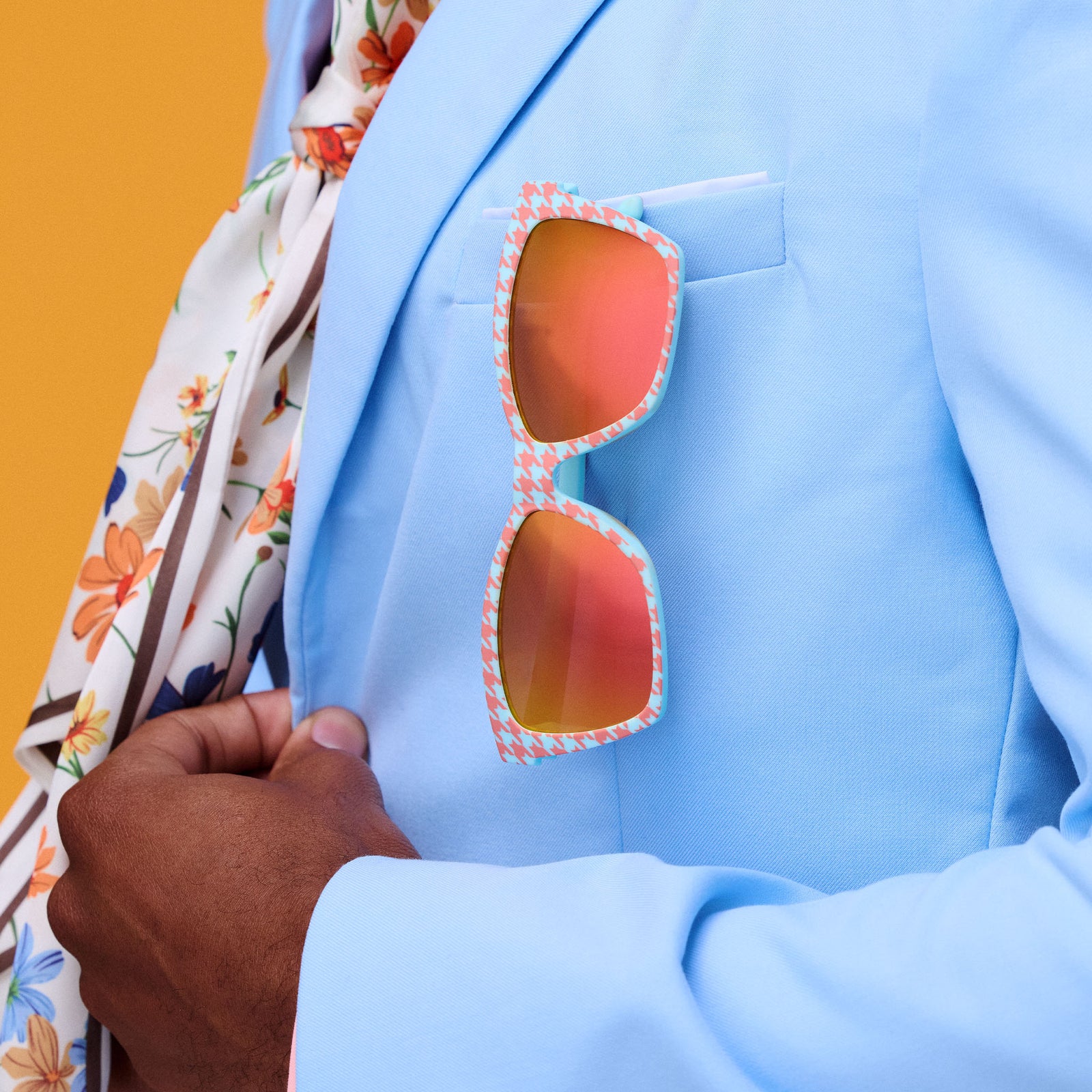 A pair of vibrant blue and burnt-orange houndstooth print Pop Gs hangs from the breast pocket of a man's light blue blazer.
