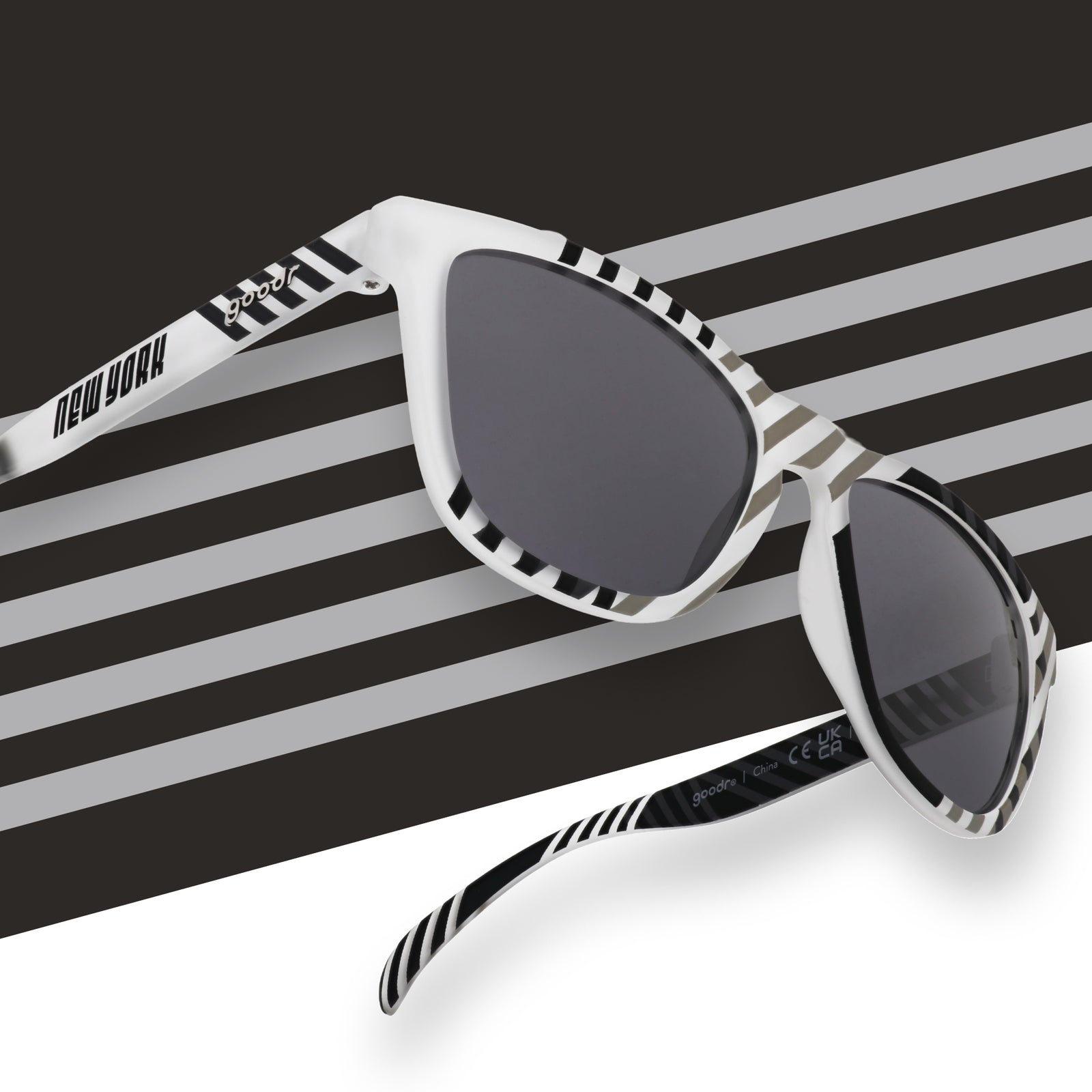 Gray and black sunglasses featuring a New York and goodr logo in front of a striped background.