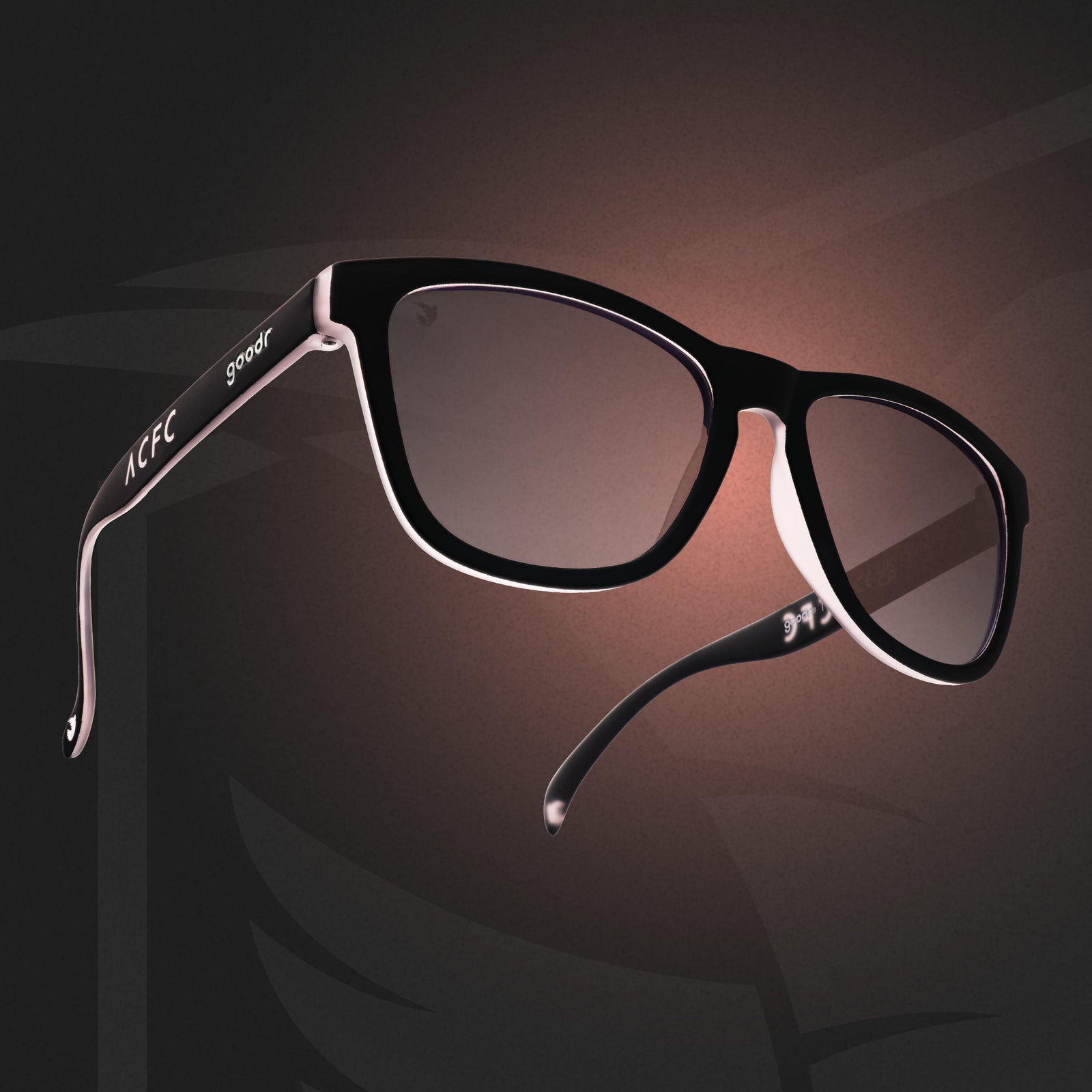 Three-quarter angle view of black and pink sunglasses with black lenses and ACFC logo on a pink and black ACFC background.