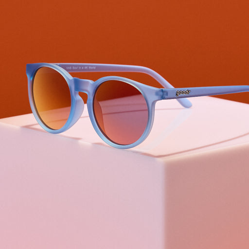 Blue sunglasses with red-tinted lenses on a pink surface against an orange background