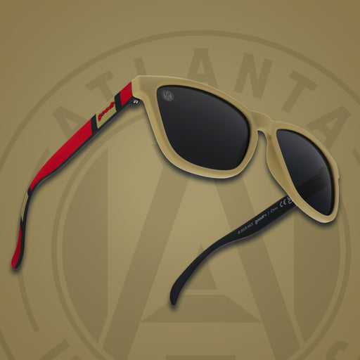 Three-quarter angle front view of MLS Atlanta United shades on a gold background. Gold+red frames. Black lenses.