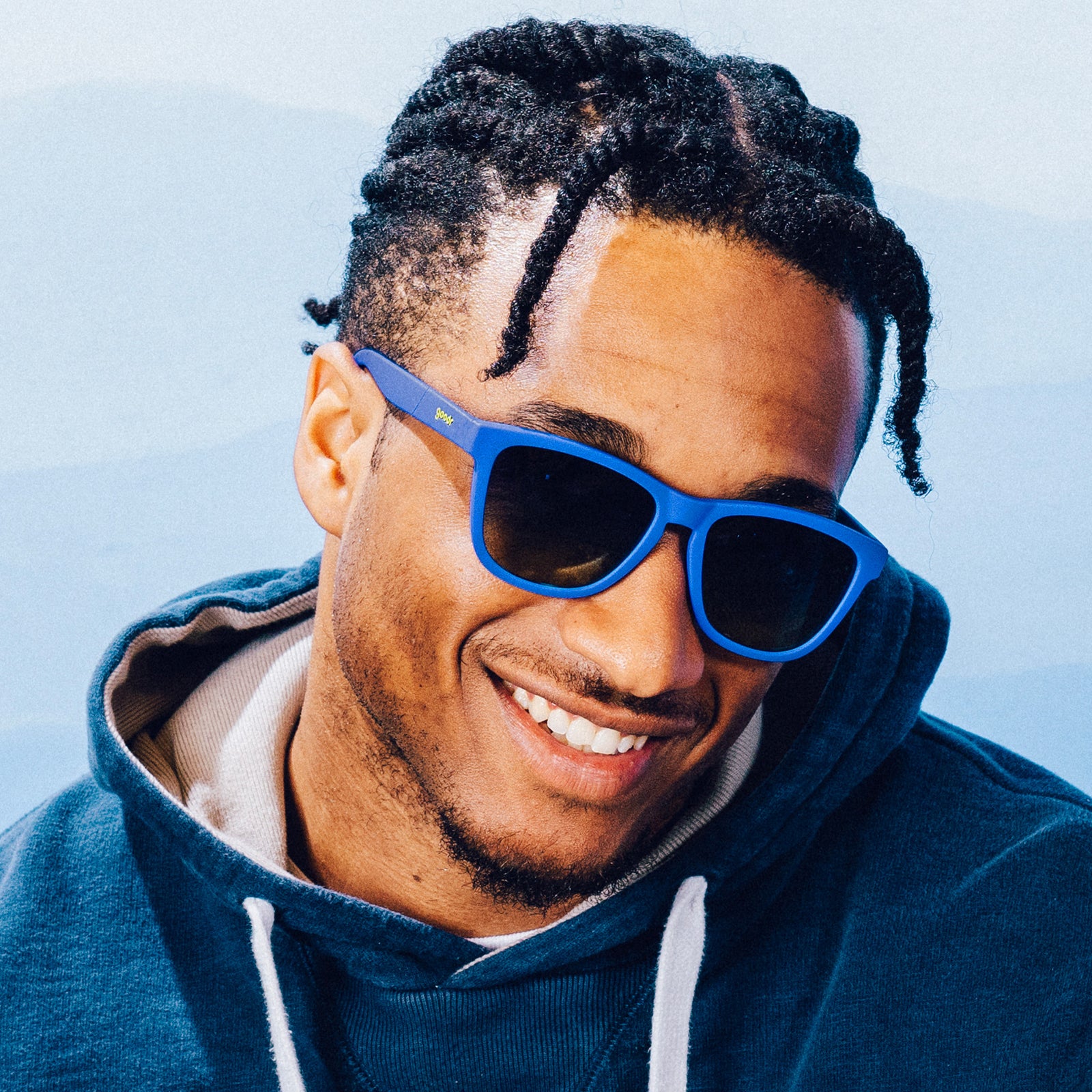 A man smiles while wearing classic blue sunglasses with blue-yellow ocean lenses.