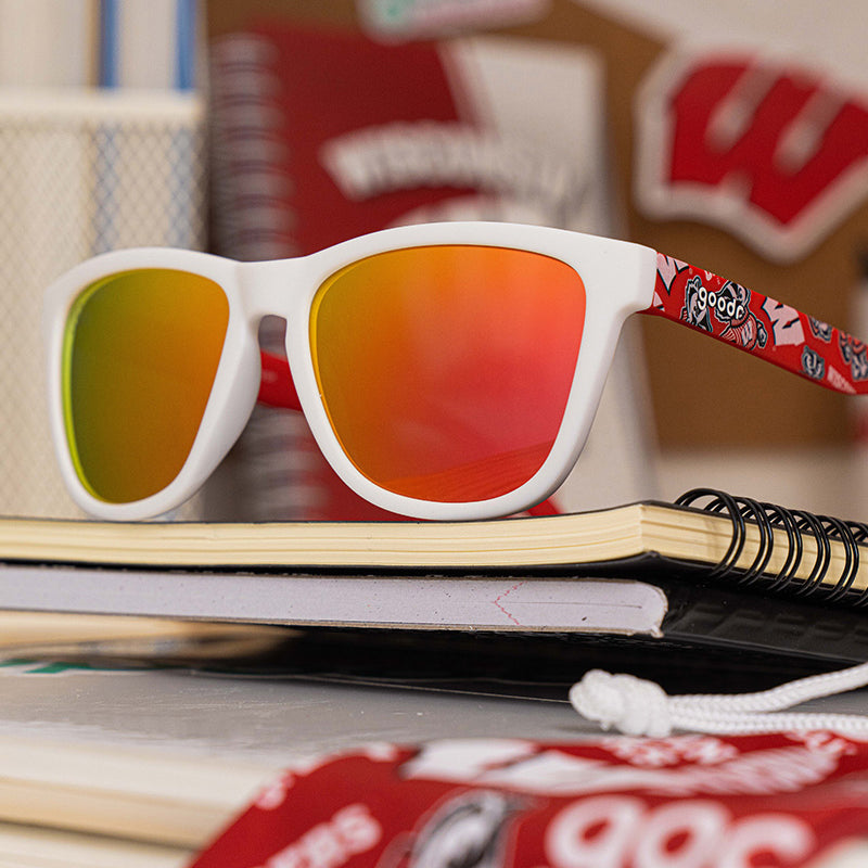 White sunglasses with rainbow lenses on a notebook among other items.