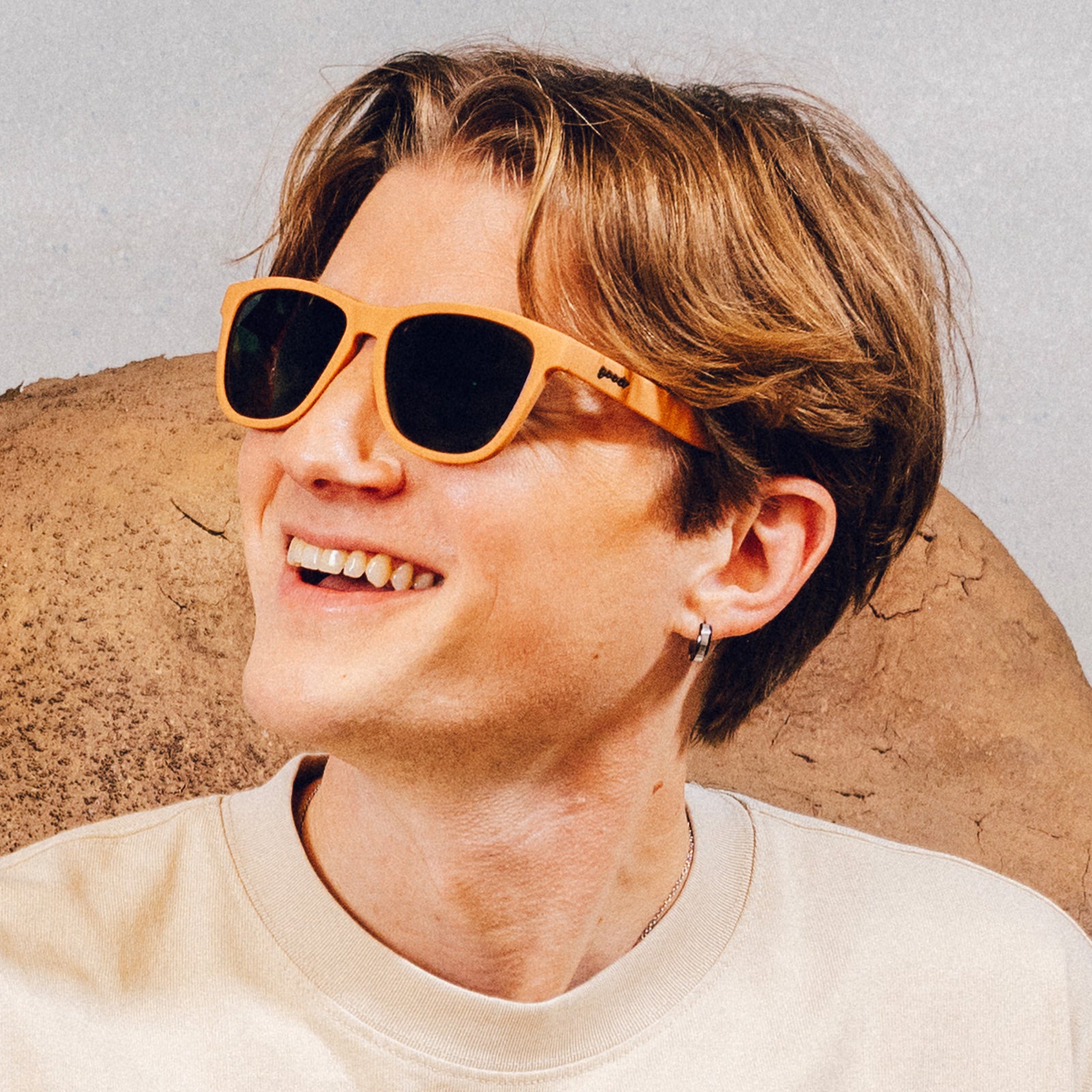 Man wearing classic brown sunglasses with green non-reflective lenses smiles in front of a desert backdrop.