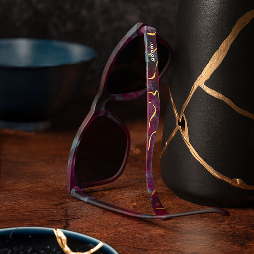 Full back view of kintsugi shades with teal lenses, purple-teal frames, and gold crack accents next to kintsugi pottery.