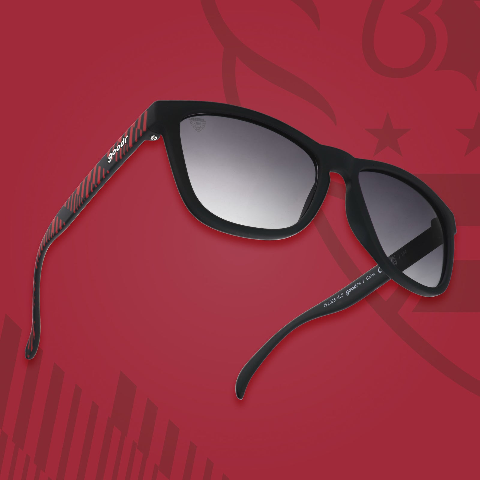 Three-quarter angle view of DC United shades tilted up. Black and red frames. Black lenses. Red background.