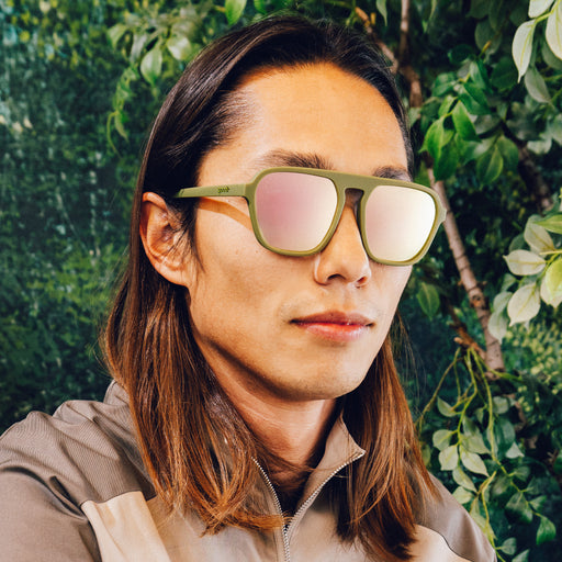 Side profile of a man wearing green retro-inspired aviator sunglasses with light pink reflective lenses.