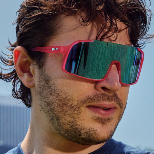 Man wearing visor sunglasses with teal reflective lenses and hot pink frames