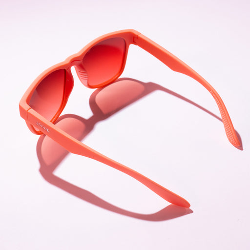 A pair of coral-colored sunglasses casting a shadow on a light pink background.