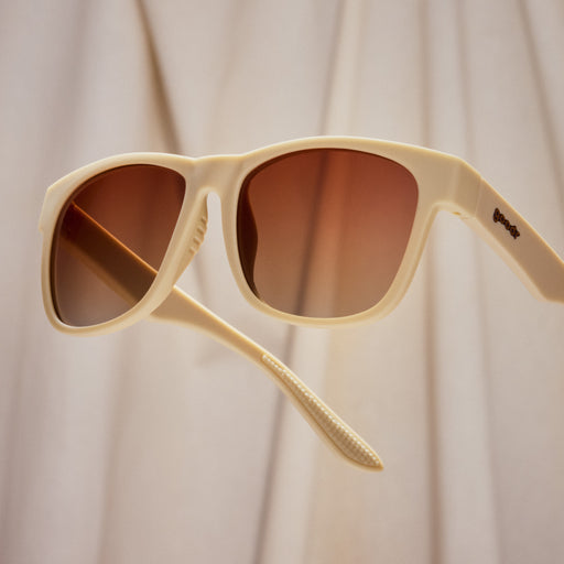 A pair of square sunglasses with light beige frames and muted orange lenses.