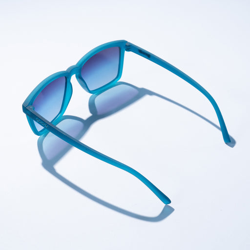 A pair of sunglasses with blue frames and lenses, sitting on a white surface/background.