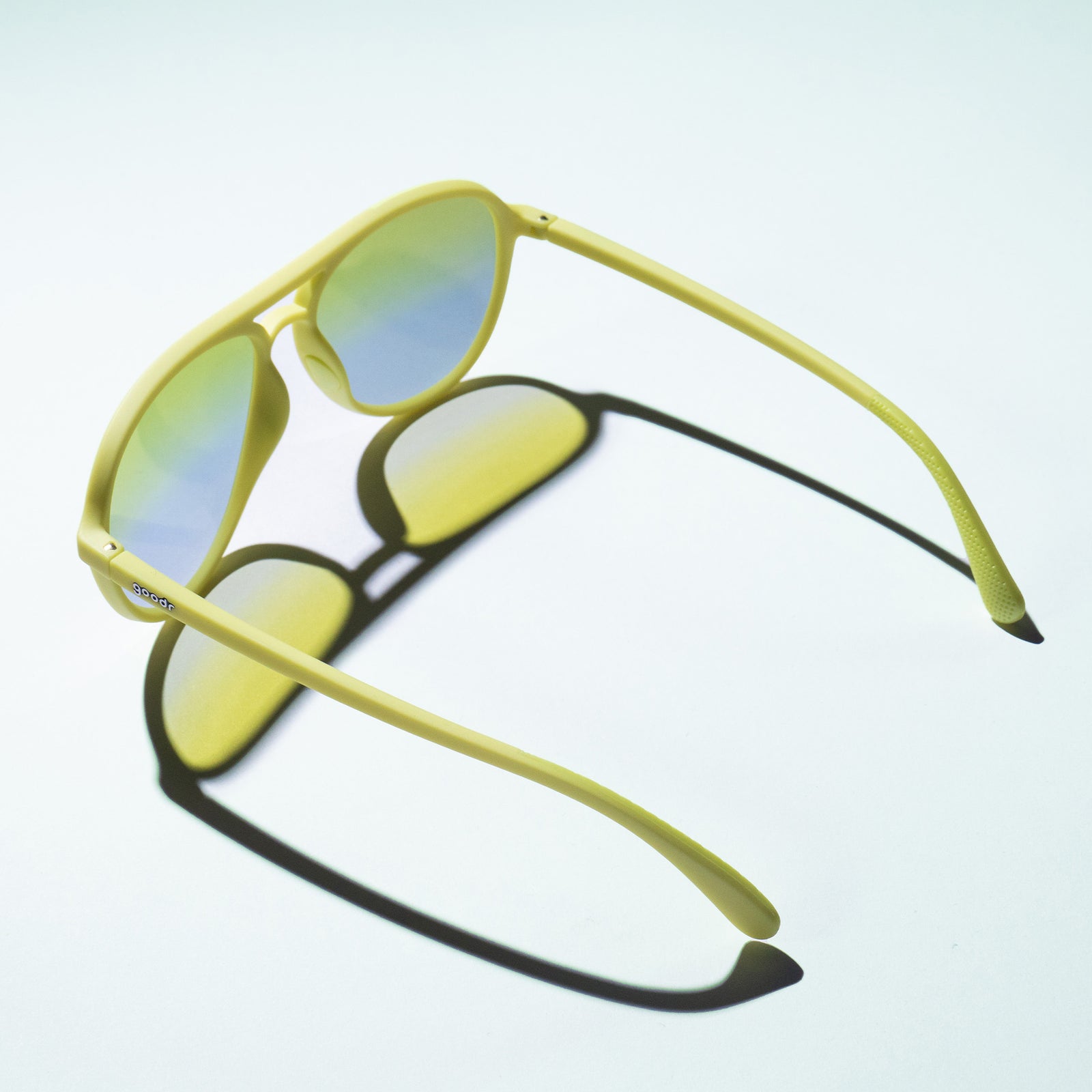 Light green-yellow aviator sunglasses with blue and green lenses on a white background, shown from a bird's eye view.