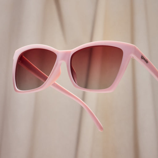 A pair of cat-eye sunglasses with light pink frames and rosy lenses.