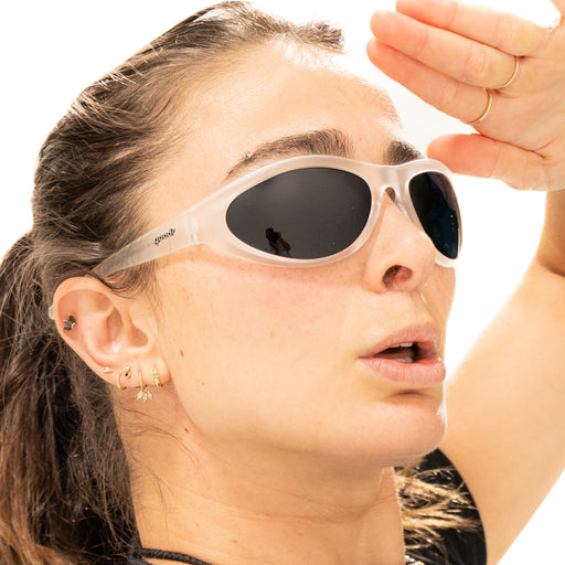 A woman wearing clear, translucent framed sunglasses with black lenses, holding a hand over her brow as if to block out sunlight.