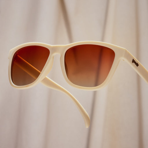 A pair of square sunglasses with light beige frames and muted orange lenses.