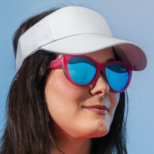 Woman wearing pink cat-eye sunglasses with blue lenses, and a white sun visor