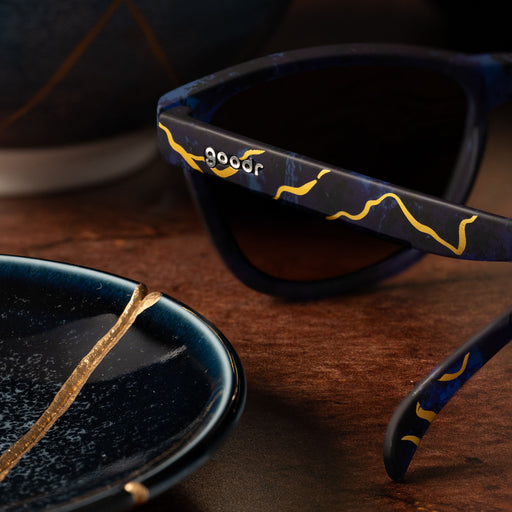 Angled back view of kintsugi shades with gold lenses, blue frames & gold crack accents on a table by kintsugi pottery.